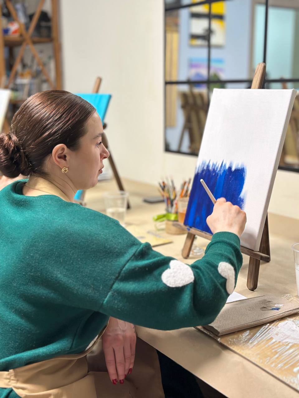Woman in green sweater with heart patches beginning a deep blue abstract painting